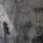 A translucent historical image of a man in a suit layered over a contemporary photo showing the dark outline of two men walking in a hallway.